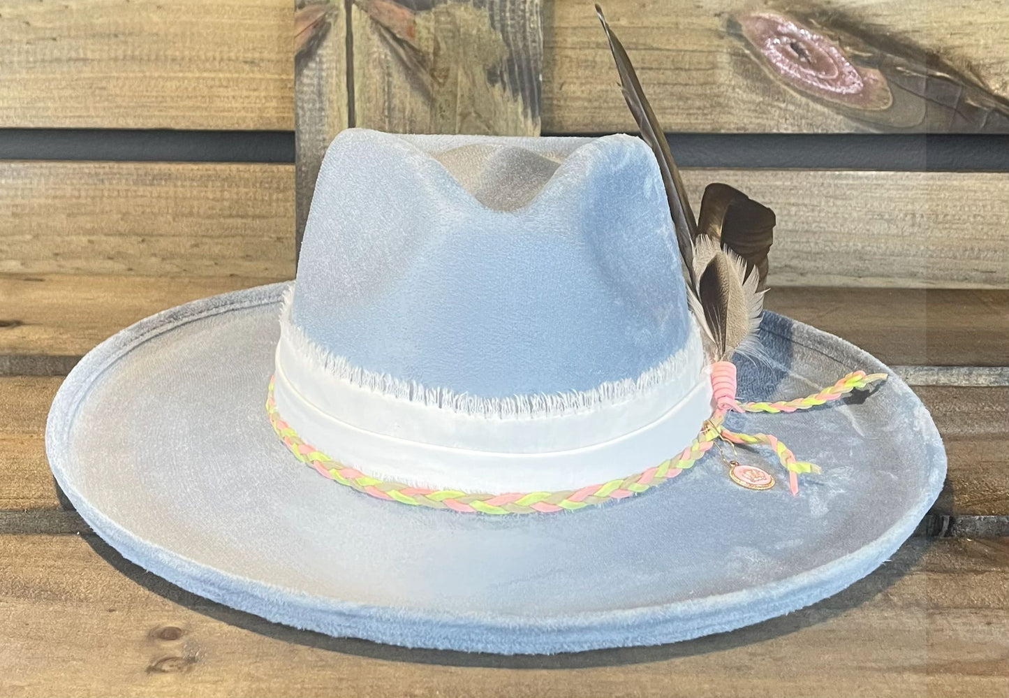 A Carolina Blue vegan suede pencil brim hat wrapped with frayed cotton and wrapped with a braided suede string. Styled with big beautiful turkey feathers and crown charm.