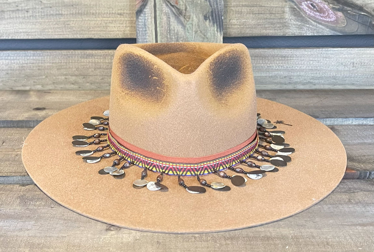 A tan Peter Grimm wide brim hat. Styled with a unique band and branded with a palm tree.