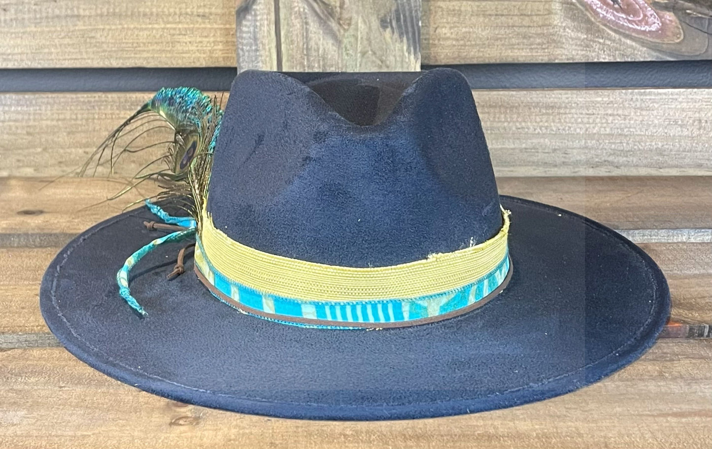 The Beckville is a navy blue flat brim vegan suede hat styled with Peacock feathers.