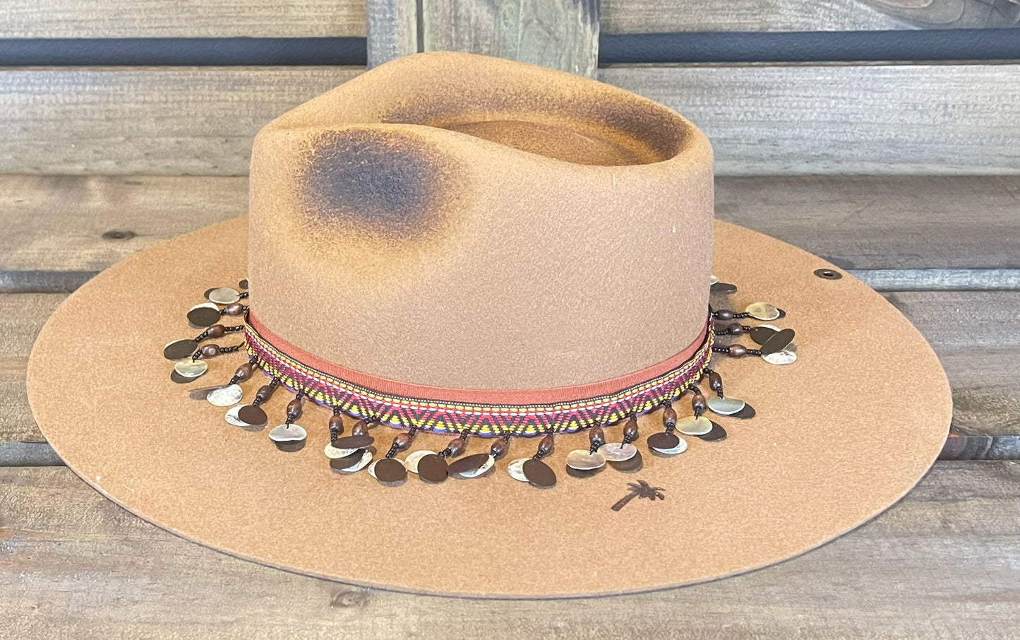 A tan Peter Grimm wide brim hat. Styled with a unique Moroccan band and branded with a palm tree.