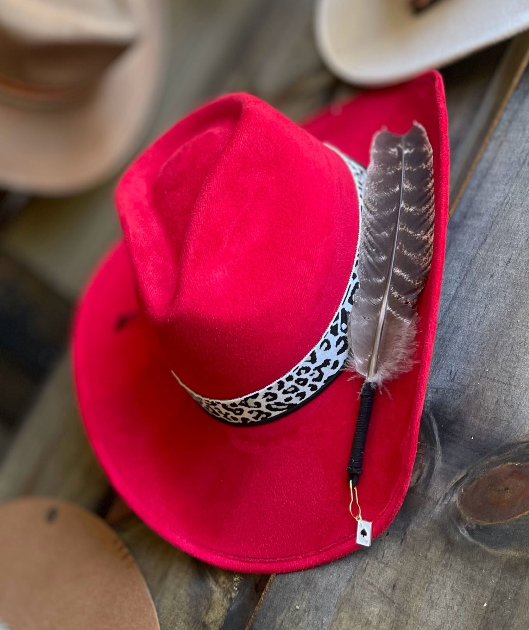 A red suede cowboy hat with a Leopard print band and styled with a large feather