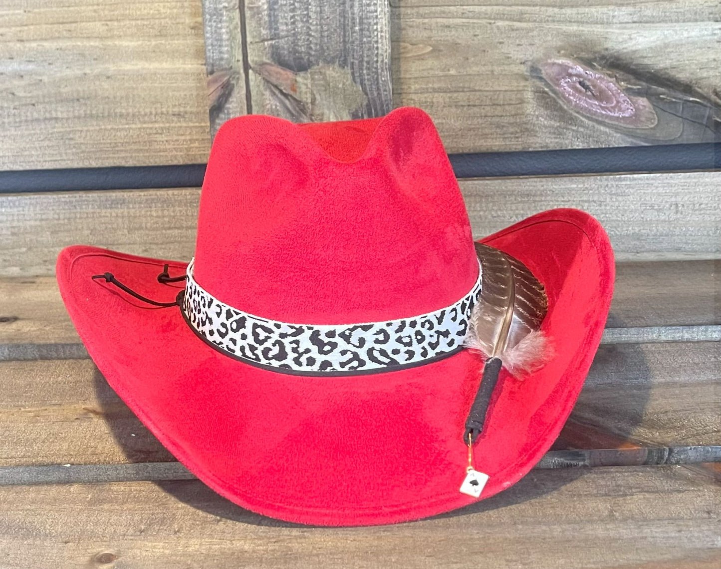 A red suede cowboy hat with a Leopard print band and styled with a large feather