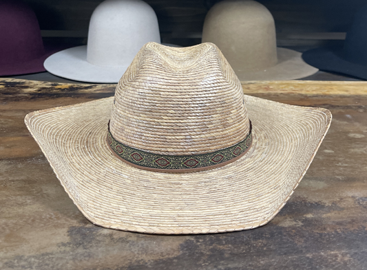 Straw hat with a decorative band on a wooden surface, with other hats in the background.
